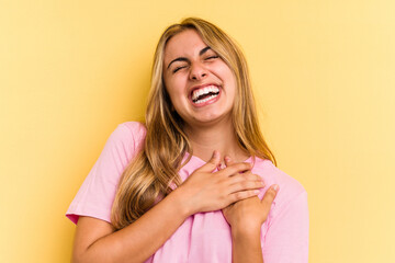 Young caucasian blonde woman isolated on yellow background  laughing keeping hands on heart, concept of happiness.