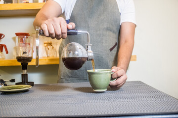 Man pouring coffee in the cup from a siphon coffee maker