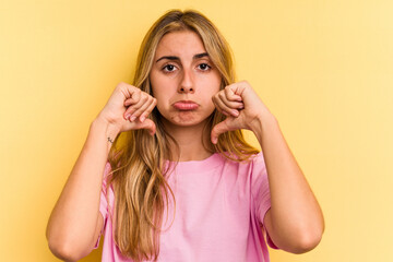Young caucasian blonde woman isolated on yellow background  showing a dislike gesture, thumbs down....