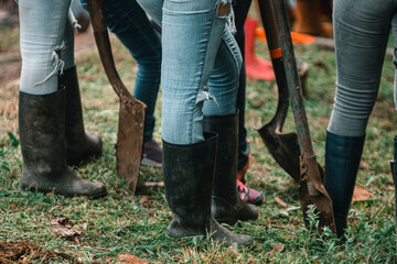 pies de personas con botas de hule y palas reunidos para sembrar plantas y reforestar