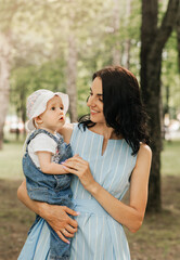 A young mother holds the little daughter infant in the park in the summer