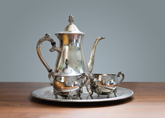 Ornate 4-piece tea set on table. Silver or silver plated tea pot, sugar bowl and cream or milk jug....