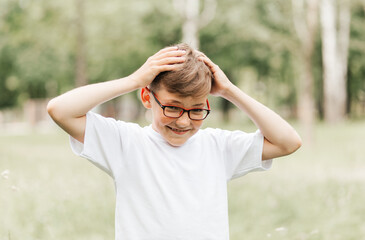 A cute freckled boy with glasses holds on to his head.