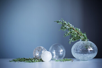 juniper branches in glass vase and christmas balls on gray background