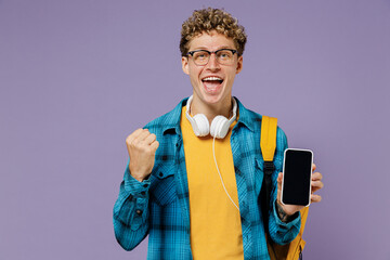 Young boy teen student in casual clothes backpack earphones glasses use mobile cell phone with blank screen workspace area do winner gesture isolated on violet background studio Education university 