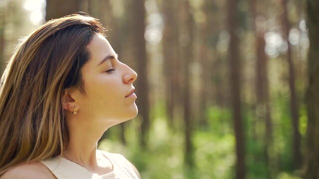 Close up portrait of a pretty young woman breathes fresh air into her full chest in the middle of pine forest on nature. Outdoor. freshness, peace and quiet. Girl with closed eyes enjoys the sounds
