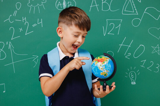 Young amazed male kid school boy 5-6 years old in t-shirt backpack hold spin Earth world globe isolated on green wall chalk blackboard background. Childhood children kids education lifestyle concept - Powered by Adobe