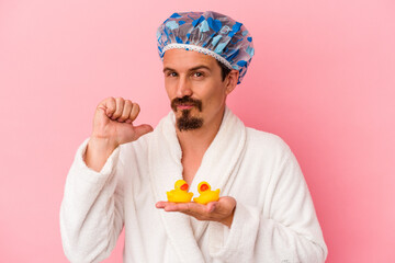 Young caucasian man going to the shower with rubber ducks isolated on pink background feels proud...