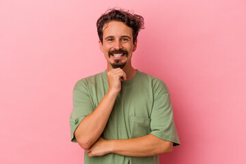 Young caucasian man isolated on pink background smiling happy and confident, touching chin with...