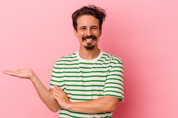Young caucasian man isolated on pink background showing a copy space on a palm and holding another...