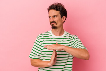 Young caucasian man isolated on pink background showing a timeout gesture.