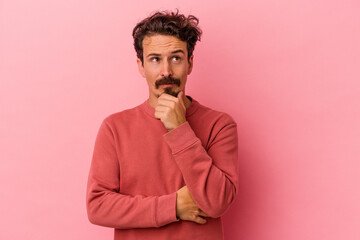Young caucasian man isolated on pink background looking sideways with doubtful and skeptical expression.