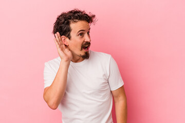 Young caucasian man isolated on pink background trying to listening a gossip.