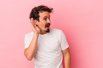 Obraz premium Young caucasian man isolated on pink background trying to listening a gossip.