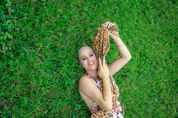 Beautiful Woman, beautiful and strong. Happy and smiling on the ranch with sensuality. Smiling and looking steady and steady. Bald and hairless. Breast cancer lying on green grass and wearing shawl.