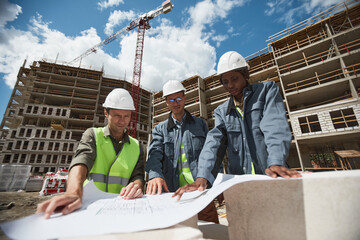Low angle portrait of three workers discussing floor plans at construction site, copy space
