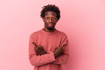 Obraz premium Young african american man isolated on pink background points sideways, is trying to choose between two options.