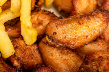 Fried chicken wings and French fries on a plate, close-up, selective focus.