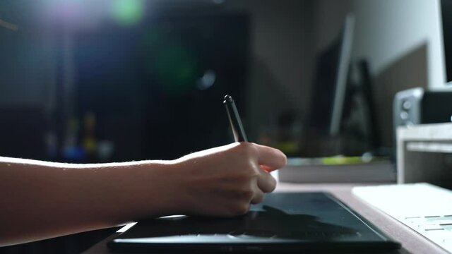 woman working on computer at home using black pen mouse drawing graphic design Close-up shot on a desk, backlit.