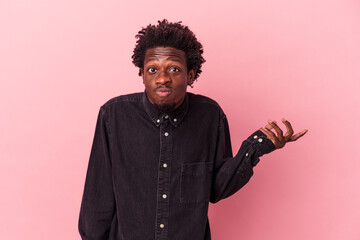 Young african american man isolated on pink background doubting and shrugging shoulders in questioning gesture.