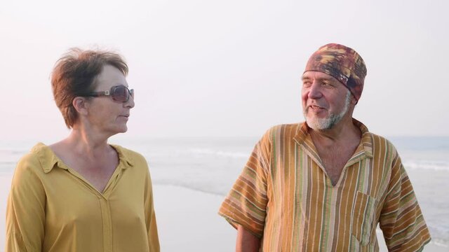 Senior couple walking on the beach at morning, smiling and talking, steadicam shot in slow motion