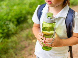 Thirsty boy holds in hands reusable green bottle with pure water. Summer outdoor recreation. Healthy lifestyle. - 452542623