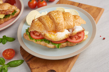 two croissant sandwiches on wooden table, top view, Sandwich with bacon, fried egg. Ham, cheese, bacon, fried egg, tomato, french fries and lettuce served in a plate.