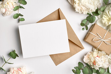 Obraz na płótnie Canvas Invitation or greeting card mockup with envelope, gift box and white peony flowers and eucalyptus twigs