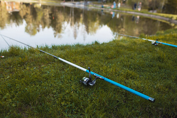 Obraz na płótnie Canvas the fishing rod lies on the green grass near the lake