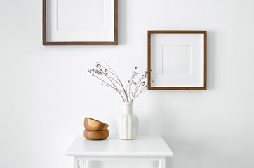 Square wooden frame mockup for artwork, photo, print and painting presentation. White walll with vase, dry twigs and wooden decorations.