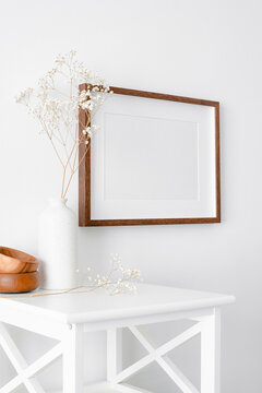 Landscape frame on white wall with furniture and dry gypsophila plant in vase. Blank frame mockup for artwork, print or photo presentation.