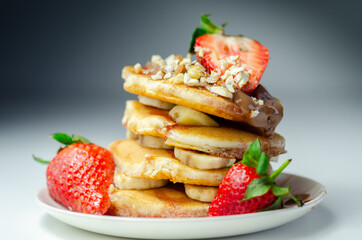 Pancakes stacked with bananas, strawberries and nuts, topped with chocolate and strawberry sauce