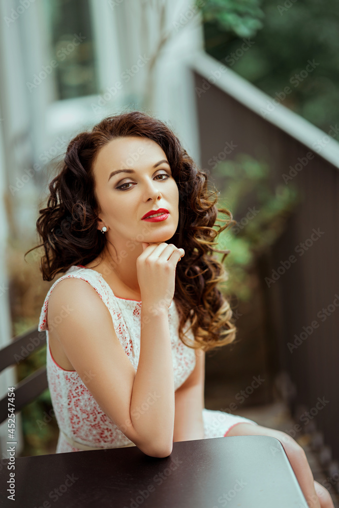 Sticker Curly Caucasian brunette woman wearing a dress sitting behind the table