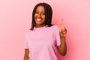 Young african american woman isolated on pink background  joyful and carefree showing a peace symbol with fingers.