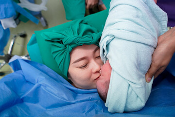 Obraz na płótnie Canvas Newborn baby in delivery room.Blurred Mother background giving birth to a baby and kiss her baby. Woman pregnant patient in a hospital. Parent and infant first moments of bonding.