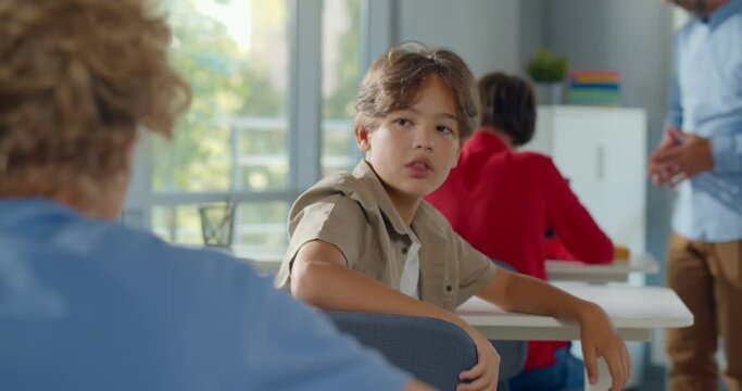Back view of schoolboy sitting at desk on exam and turn around talking to classmate