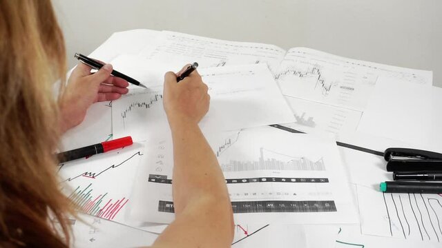 Woman investor at work examines paper with stock charts.