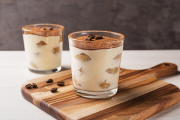 Homemade Italian tiramisu dessert with cocoa powder in glasses on light wooden table.