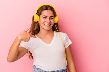 Young caucasian woman listening to music isolated on pink background  person pointing by hand to a shirt copy space, proud and confident