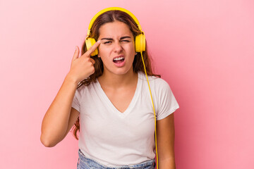 Young caucasian woman listening to music isolated on pink background  showing a disappointment gesture with forefinger.