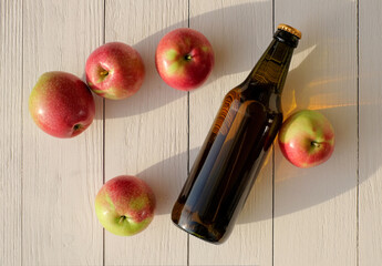 Bottle of cider near autumn apples on wooden background, top view