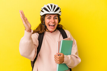 Young caucasian student woman wearing a bike helmet isolated on yellow background  receiving a pleasant surprise, excited and raising hands.