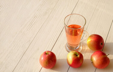 Glass cup of cider or lemonade and apples on wooden background with natural sunlight, copy space
