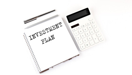 Notepad with text INVESTMENT PLAN with calculator and pen. White background. Business concept