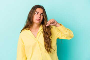 Young caucasian woman isolated on blue background  showing a dislike gesture, thumbs down....