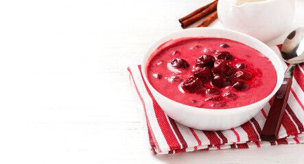 Sour cherry soup in a white bowl on a white background. Hungarian cold cherry soup with cream or sour cream, sugar and cinnamon. Sweet summer soup. Free space for text.