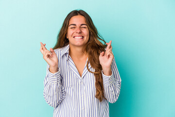 Young caucasian woman isolated on blue background  crossing fingers for having luck