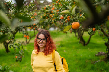 Red-haired smiling woman stands in the tangerine garden.