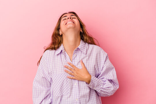 Young caucasian woman isolated on pink background  laughs out loudly keeping hand on chest.