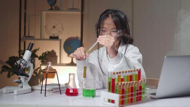 Young Asian Scientist Girl With Dirty Face Mixes Chemicals In Test Tube And Work With Laptop Computer. Child Learn With Interest
